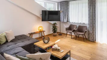 Gemütliches Wohnzimmer mit Holzboden, bequemer Eckcouch und Fernseher an der Wand.