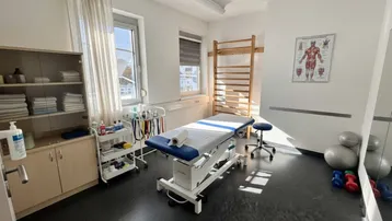 Heller Therapieraum mit Behandlungsliege, Sprossenwand und medizinischen Geräten für physiotherapeutische Anwendungen.