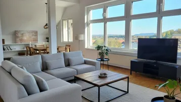 Helles und geräumiges Wohnzimmer mit bequemer Couch, Holzboden und weitem Blick ins Grüne.