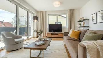 Helles Wohnzimmer mit modernem Sofa, Teppich und Zugang zum Balkon.