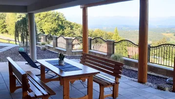 Überdachte Terrasse mit Holztisch und Bänken, bietet einen weiten Blick auf die grüne Landschaft.