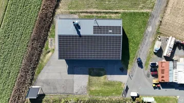 Senkrechte Luftaufnahme eines Betriebsgebäudes mit Photovoltaikanlage auf dem Dach, umgeben von Grünflächen.