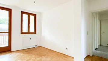 Helles Wohnzimmer mit klassischem Parkettboden und Zugang zu einem Balkon.