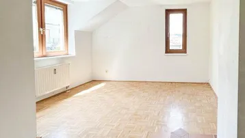 Geräumiger Wohnbereich mit Parkettboden und einem Bereich mit Terrakottafliesen, hell durch große Fenster.