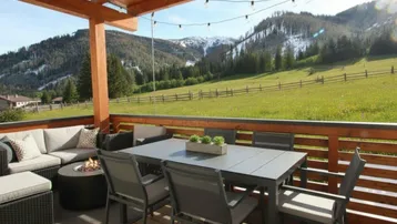Geräumige Terrasse mit modernen Gartenmöbeln, Feuerstelle und atemberaubendem Blick auf die Berge und grüne Wiesen.