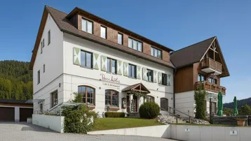 Traditionelles Gebäude im alpinen Stil mit weißer Fassade, Holzdetails und grünen Fensterläden.