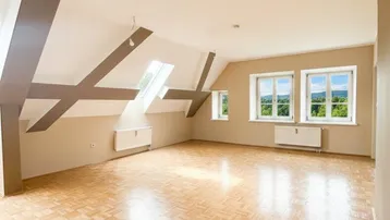 Helles Dachgeschosszimmer mit Parkettboden, sichtbaren Holzbalken und weitem Blick ins Grüne.