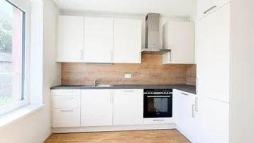 Helle, moderne Küche mit weißen Schränken, Holzakzenten und Parkettboden, gut beleuchtet durch ein großes Fenster.