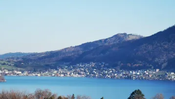 Weitläufiger Blick über einen See und die umliegende Landschaft mit bewaldeten Hügeln.