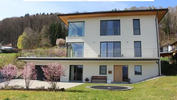 Modernes Einfamilienhaus mit mehreren Balkonen, Garage und Gartenbereich in Hanglage.