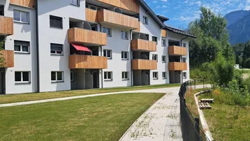 Modernes Mehrfamilienhaus mit Holzverkleidung an den Balkonen und gepflegter Grünfläche.
