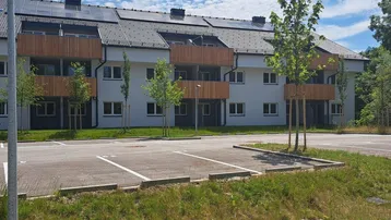 Modernes Mehrfamilienhaus mit Holzverkleidung, Solarpaneelen auf dem Dach und Außenparkplätzen.