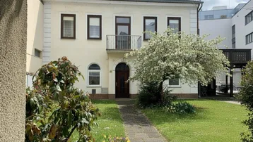 Vorderansicht des Hauses mit blühendem Baum, kleinem Vorgarten und Zugang zum Eingangsbereich.