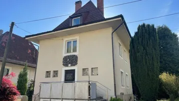 Vorderansicht des Hauses mit heller Fassade, Satteldach und einem kleinen Balkon im Eingangsbereich.