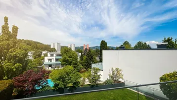 Weitläufiger Blick von der Terrasse auf einen grünen Garten mit Pool und die umliegende Wohnbebauung unter blauem Himmel.