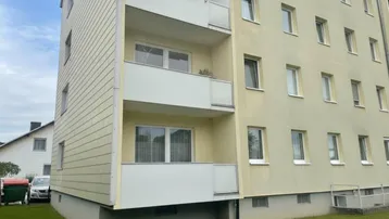 Seitenansicht eines Mehrfamilienhauses mit Balkonen und gepflegter Rasenfläche.