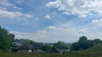 Weitläufige grüne Landschaft mit vereinzelten Häusern unter einem bewölkten Himmel.