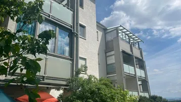 Seitenansicht des Gebäudes mit mehreren Balkonen, Glasgeländern und üppigem Grün.
