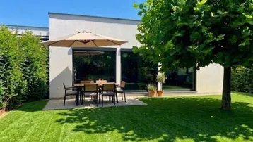 Moderne Terrasse mit Esstisch, Sonnenschirm und gepflegtem Rasen vor dem Haus.