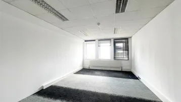 Geräumiges, leeres Büro mit Teppichboden und großen Fenstern, bereit zur individuellen Gestaltung.