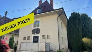 Gepflegtes Einfamilienhaus mit beigefarbener Fassade, Mansarddach und kleinem Balkon am Eingang.