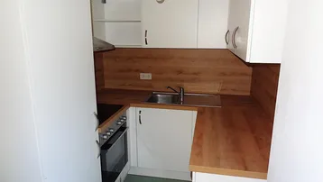 Kleine Einbauküche mit weißen Schränken, Holz-Arbeitsplatten und integriertem Herd.