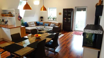 Geräumiger offener Wohn- und Essbereich mit Holzboden, beiger Eckcouch und Zugang zum Balkon.