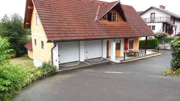 Gelbes Einfamilienhaus mit rotem Ziegeldach, Doppelgarage und gepflasterter Auffahrt.