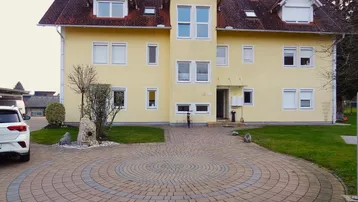 Gelbes Mehrfamilienhaus mit rotem Dach und gepflasterter Auffahrt in ländlicher Umgebung.