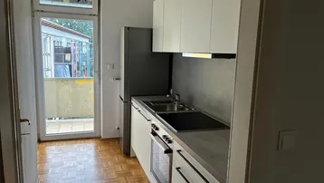 Moderne Küchenzeile mit integrierten Geräten und Zugang zu einem kleinen Balkon.