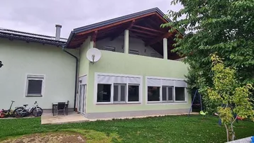 Grünes Haus mit Balkon, Garten und Solaranlage auf dem Dach.