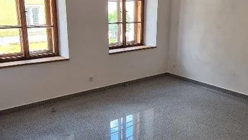 Heller Raum mit sichtbaren Holzbalken, Steinfliesenboden und zwei Fenstern.