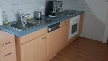Helle Küche mit Holzschränken, blauer Arbeitsplatte und integrierten Geräten unter Dachschräge.