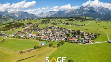 Weitläufiger Panoramablick auf ein idyllisches Dorf mit grünen Wiesen und majestätischen Bergen.