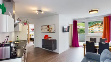 Heller offener Wohnbereich mit integrierter Küche, Essbereich und Zugang zum Balkon mit Bergblick.