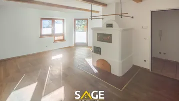 Helles Wohnzimmer mit Holzbalken, Parkettboden und traditionellem Kachelofen, mit Zugang zum Außenbereich.