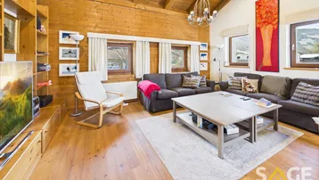 Gemütliches Wohnzimmer im alpinen Stil mit Holzwänden, Holzbalkendecke und Blick auf die Berge.