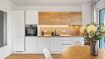 Moderne Einbauküche mit weißen und holzfarbenen Fronten, integrierten Geräten und Essbereich.