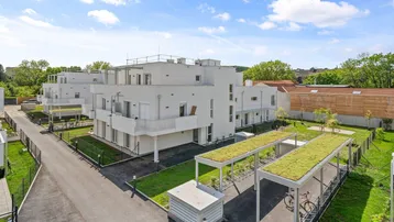 Moderne Wohnanlage mit weißen Fassaden und begrünten Carports unter blauem Himmel.