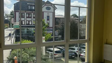 Heller Innenraum mit großen Fenstern, die einen Blick auf die Straße und gegenüberliegende Gebäude bieten.