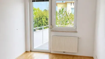 Helles Zimmer mit Parkettboden, großem Fenster und Zugang zu einem französischen Balkon.