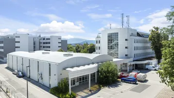 Luftaufnahme eines modernen Büro- und Lagerkomplexes mit Parkplätzen unter blauem Himmel.