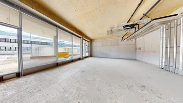 Unfertiger Innenraum mit großen Fenstern, Betonwänden und sichtbaren Installationen, bereit für den Ausbau.