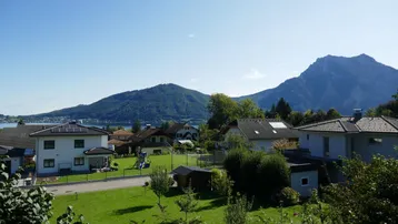 Panoramablick über eine Wohnsiedlung mit grünen Gärten, einem See und majestätischen Bergen im Hintergrund.