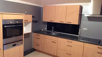 Moderne Küche mit hellen Holzfronten, integrierten Geräten und dunkler Arbeitsplatte.