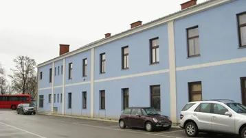 Blau gestrichenes Mehrfamilienhaus mit Parkplätzen davor unter bewölktem Himmel.