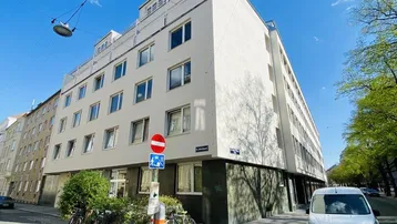 Gebäudeansicht von außen an einer Straßenecke mit weißer Fassade und blauer Himmel.