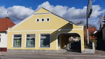 Gelbes Gebäude mit Giebeldach und einem überdachten Eingangsbereich an einer Straße.