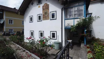 Weißes Haus mit traditioneller Fassadenmalerei, kleinem Vorgarten und überdachtem Eingangsbereich.