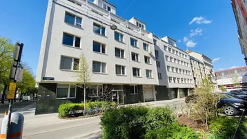Modernes Mehrfamilienhaus mit weißer Fassade und vielen Fenstern an einer städtischen Straße.
